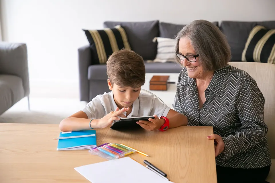 Een oma kijkt mee terwijl haar kleinzoon iets op een tablet laat zien